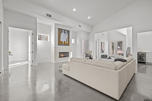 living room featuring high vaulted ceiling, a stone fireplace, wine cooler, and concrete floors