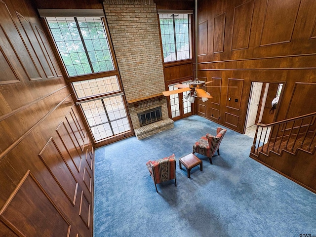 living room with wooden walls, carpet, a brick fireplace, and a ceiling fan