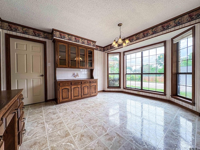 unfurnished dining area with baseboards, a chandelier, a textured ceiling, and wallpapered walls