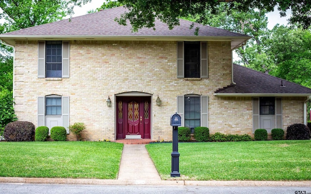 view of front of property with brick siding, a shingled roof, and a front yard