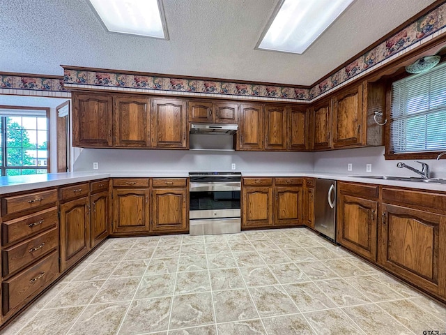 kitchen with a sink, a textured ceiling, appliances with stainless steel finishes, light countertops, and under cabinet range hood