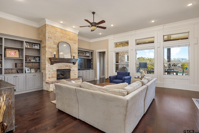 living room featuring dark wood-style floors, recessed lighting, crown molding, and a stone fireplace