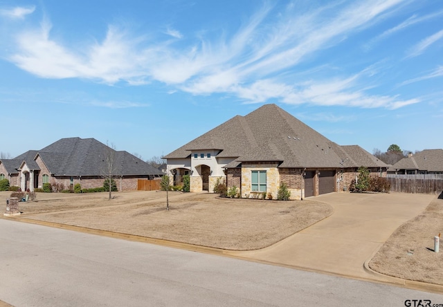 french country style house with a shingled roof, concrete driveway, fence, and an attached garage