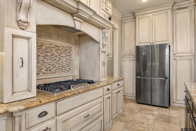 kitchen featuring tasteful backsplash, light stone countertops, cream cabinets, and stainless steel appliances