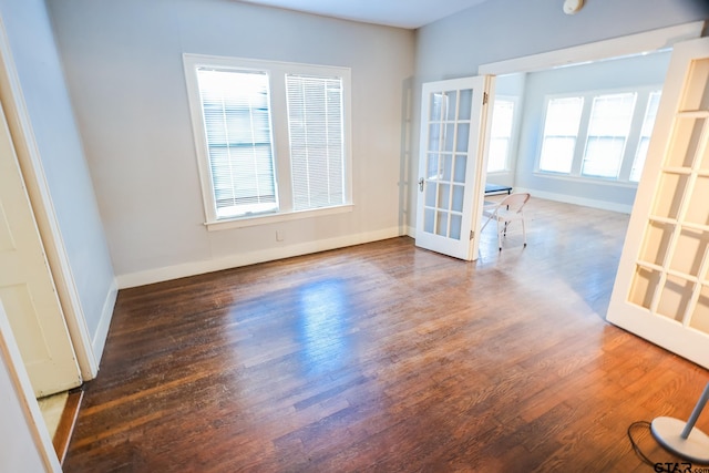 empty room with a wealth of natural light, dark hardwood / wood-style flooring, and french doors