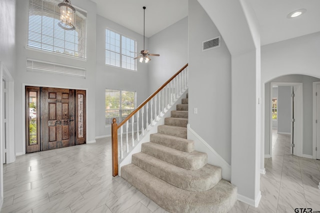 foyer featuring ceiling fan with notable chandelier and a towering ceiling