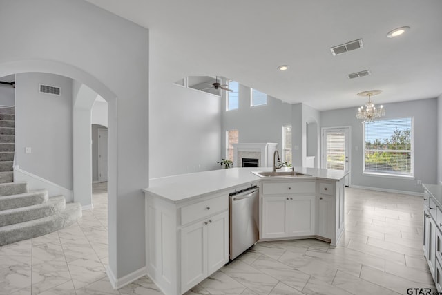 kitchen featuring ceiling fan with notable chandelier, hanging light fixtures, sink, stainless steel dishwasher, and white cabinetry