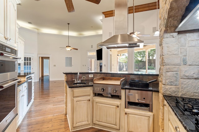 kitchen with a sink, island range hood, ceiling fan, light wood finished floors, and a high ceiling