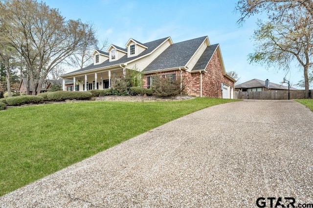 cape cod house with covered porch, a front yard, a garage, gravel driveway, and brick siding