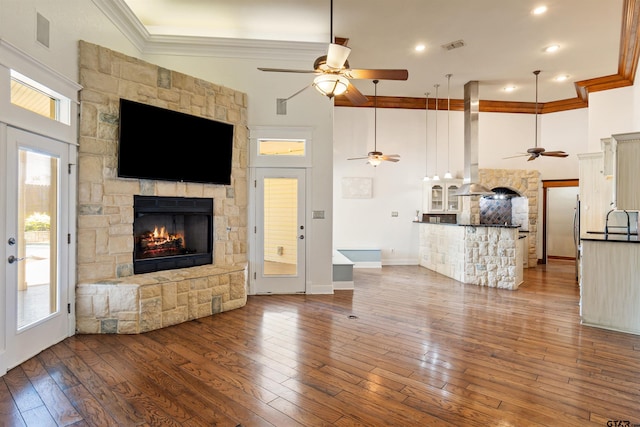 unfurnished living room featuring crown molding, a ceiling fan, a stone fireplace, hardwood / wood-style floors, and a high ceiling