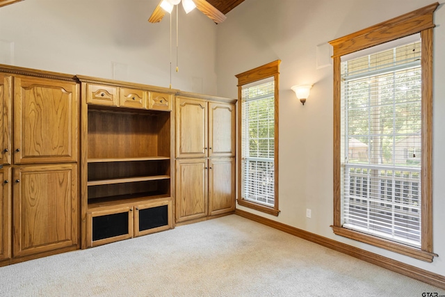unfurnished living room featuring light colored carpet, ceiling fan, baseboards, and a towering ceiling