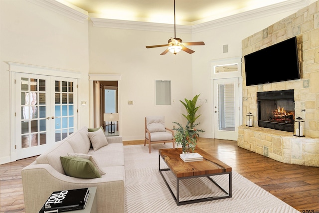 living area featuring light wood-type flooring, french doors, a stone fireplace, and ceiling fan