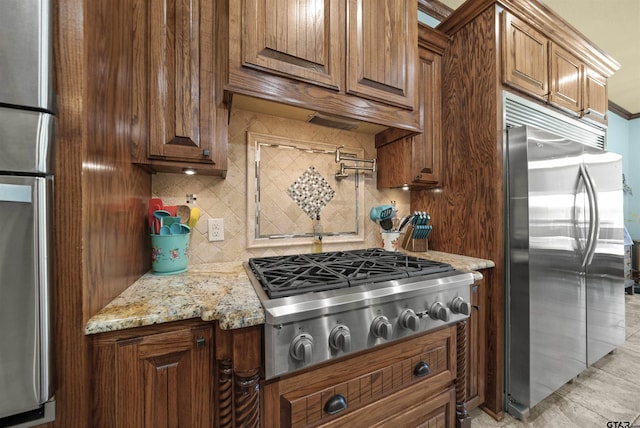 kitchen with stainless steel appliances, light tile patterned flooring, backsplash, and light stone counters