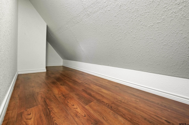 additional living space with dark wood-type flooring, lofted ceiling, and a textured ceiling