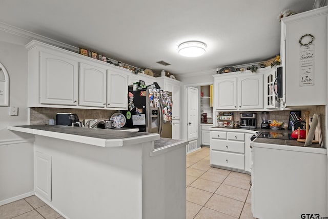 kitchen with tile counters, light tile patterned floors, kitchen peninsula, stainless steel fridge, and white cabinets