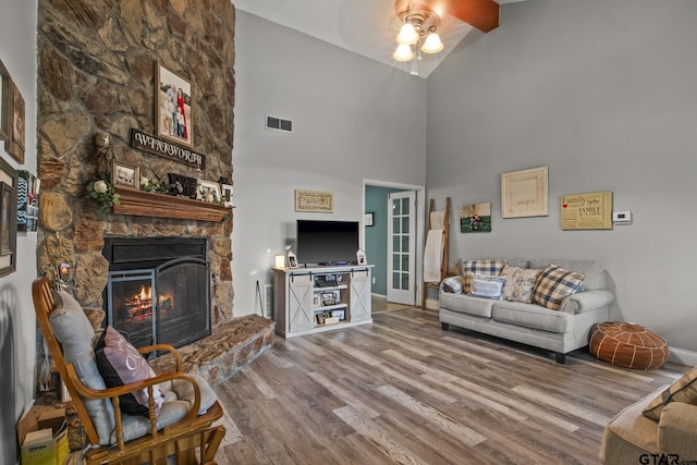 living room featuring ceiling fan, wood-type flooring, beam ceiling, high vaulted ceiling, and a stone fireplace