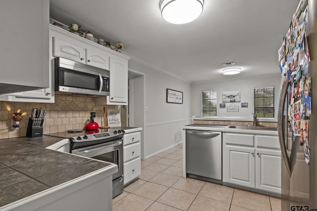 kitchen featuring appliances with stainless steel finishes, tasteful backsplash, crown molding, white cabinets, and light tile patterned flooring