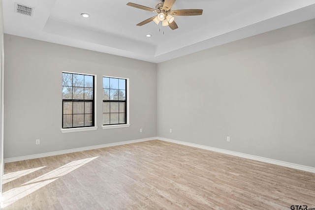 empty room featuring ceiling fan, a raised ceiling, and light wood-type flooring