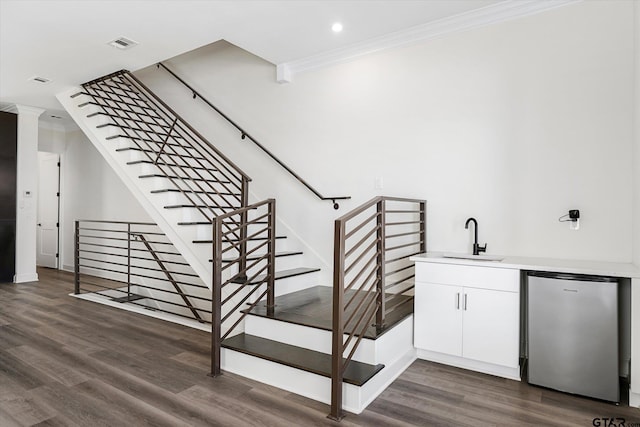 staircase featuring wet bar, hardwood / wood-style flooring, ornate columns, and crown molding