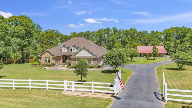 view of front of property with driveway, stone siding, a fenced front yard, a gate, and a front yard