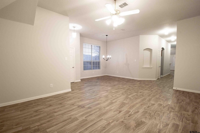 empty room featuring visible vents, baseboards, wood finished floors, and ceiling fan with notable chandelier