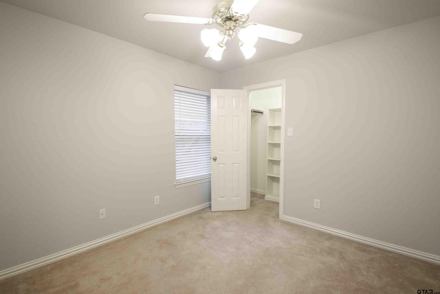 unfurnished bedroom featuring a walk in closet, baseboards, carpet, and a ceiling fan