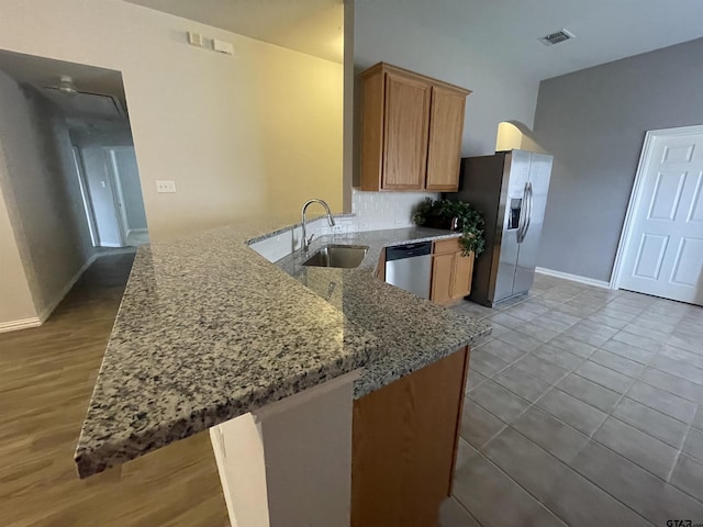 kitchen featuring visible vents, light stone countertops, appliances with stainless steel finishes, a peninsula, and a sink