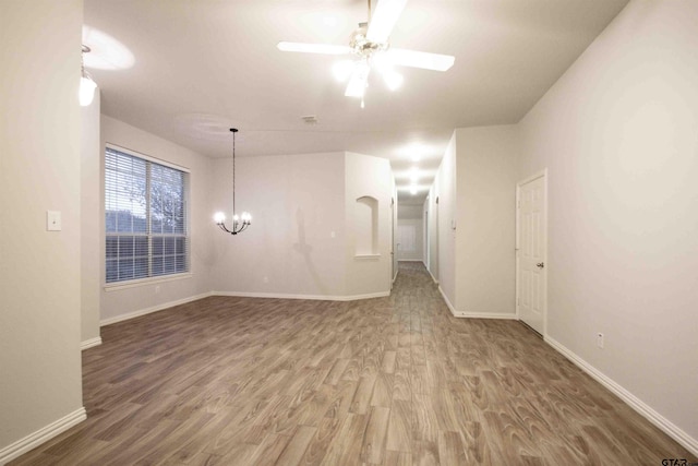 spare room featuring baseboards, wood finished floors, and ceiling fan with notable chandelier