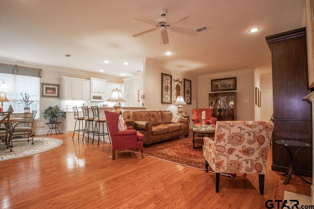 living room with light hardwood / wood-style floors, ceiling fan, and ornamental molding