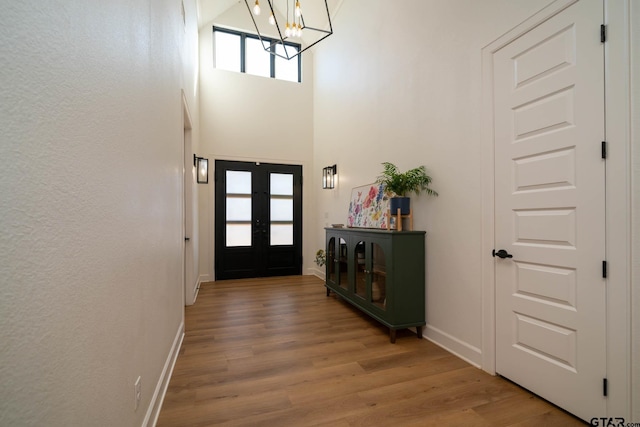 foyer with hardwood / wood-style flooring, a notable chandelier, a high ceiling, and french doors