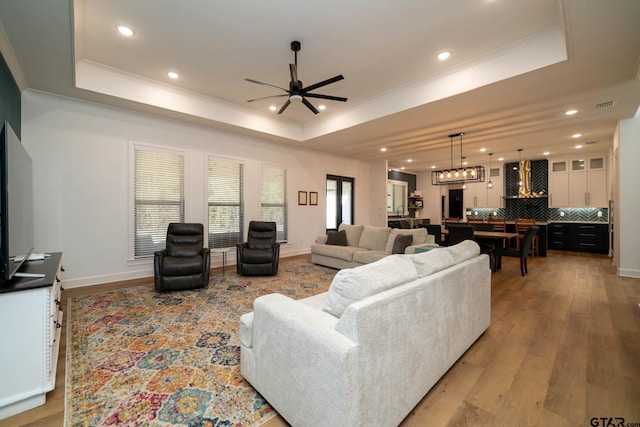 living room featuring hardwood / wood-style flooring, a raised ceiling, and ceiling fan