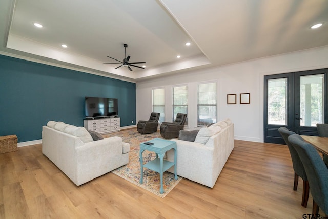 living room featuring french doors, a raised ceiling, light hardwood / wood-style flooring, ceiling fan, and ornamental molding