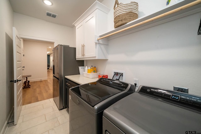 laundry room featuring washer and clothes dryer, light hardwood / wood-style floors, and cabinets