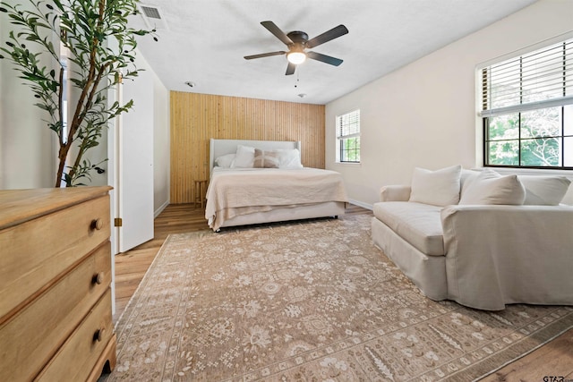 bedroom with ceiling fan, wood walls, and wood-type flooring