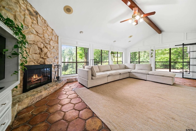 unfurnished living room with a stone fireplace, ceiling fan, a healthy amount of sunlight, and vaulted ceiling with beams