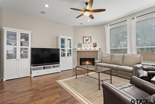 living room with ceiling fan, a tiled fireplace, and dark hardwood / wood-style flooring