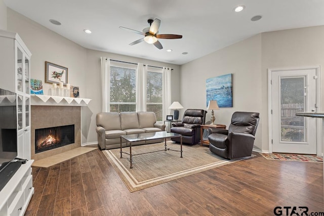 living room with dark wood-type flooring, a tile fireplace, and ceiling fan