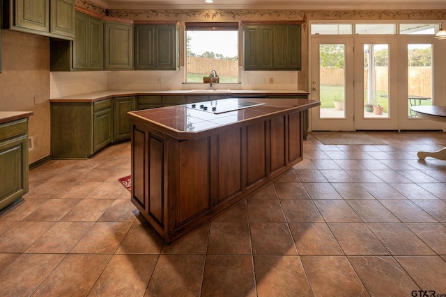 kitchen with tile patterned flooring, black electric cooktop, a kitchen island, green cabinets, and sink