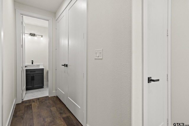 hallway featuring baseboards, dark wood finished floors, and a sink