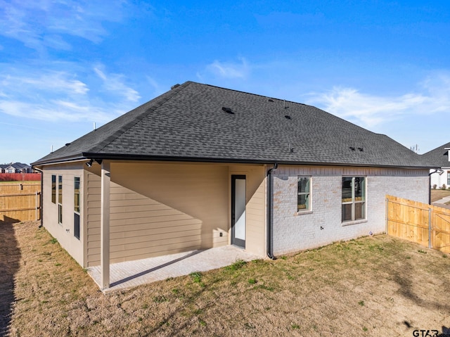 rear view of property featuring a shingled roof, a patio, fence, a yard, and brick siding