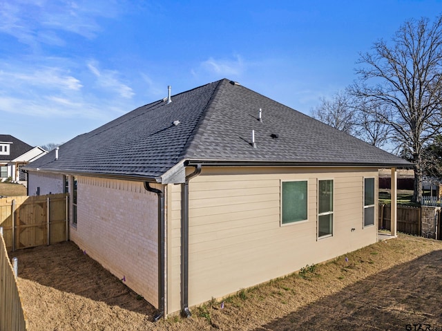 view of home's exterior featuring a shingled roof, brick siding, and fence