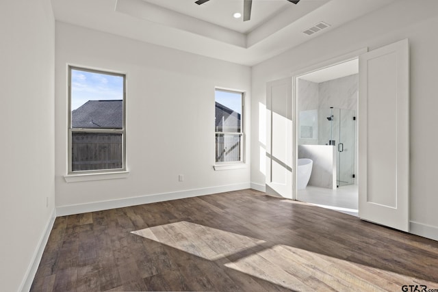 unfurnished bedroom with baseboards, a tray ceiling, visible vents, and wood finished floors