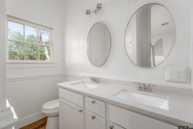 bathroom featuring toilet, double vanity, a sink, and wood finished floors