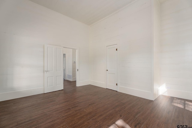 spare room with dark wood-style flooring, a towering ceiling, and baseboards