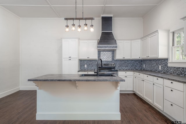 kitchen with dark countertops, dark wood-type flooring, a sink, an island with sink, and premium range hood