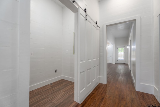 corridor with a barn door, baseboards, and dark wood-type flooring