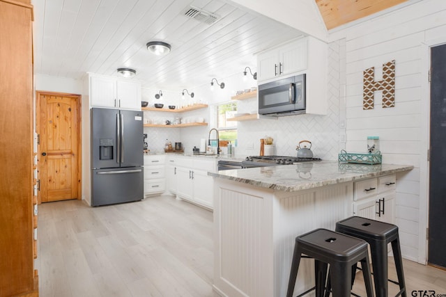 kitchen with white cabinets, a breakfast bar area, black fridge with ice dispenser, and kitchen peninsula