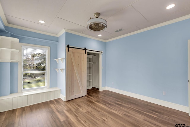 unfurnished bedroom featuring wood-type flooring, a barn door, ceiling fan, crown molding, and a closet