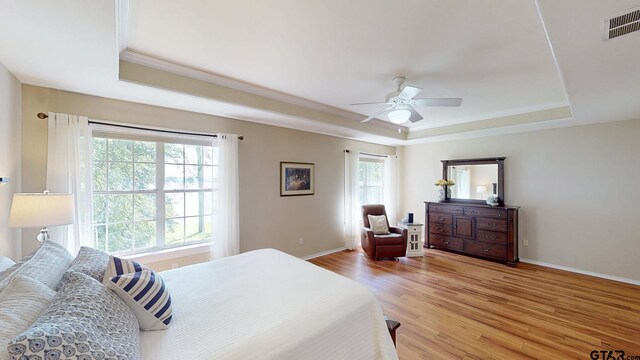 bedroom featuring light wood-style flooring, a tray ceiling, visible vents, baseboards, and a ceiling fan
