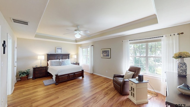 bedroom featuring a tray ceiling, light wood-style floors, visible vents, and baseboards